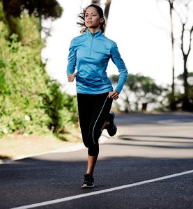 A woman jogging outdoors in sporty attire on a sunny day.